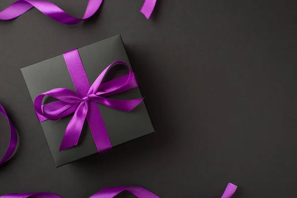 上图为黑色礼品盒 用紫色丝带包裹 在黑色背景上的弓形图案 — 图库照片
