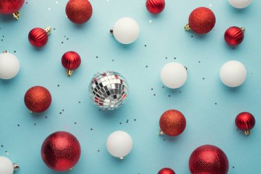 Beyaz ve kırmızı noel ağacı süslemelerinin en üstteki fotoğrafı izole edilmiş pastel mavi arka planda disko topları ve pulları