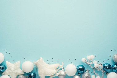 Beyaz mavi ve gümüş yılbaşı ağacı süslemelerinin en üst görüntüsü yıldız topları buz patenleri ve izole edilmiş pastel mavi arka planda karlı dallar