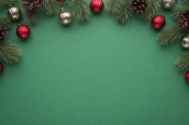 Kırmızı ve gümüş noel ağacı toplarının en üstteki görüntüsü. Çam dalları üzerinde ve koni ile izole edilmiş yeşil zemin üzerinde.