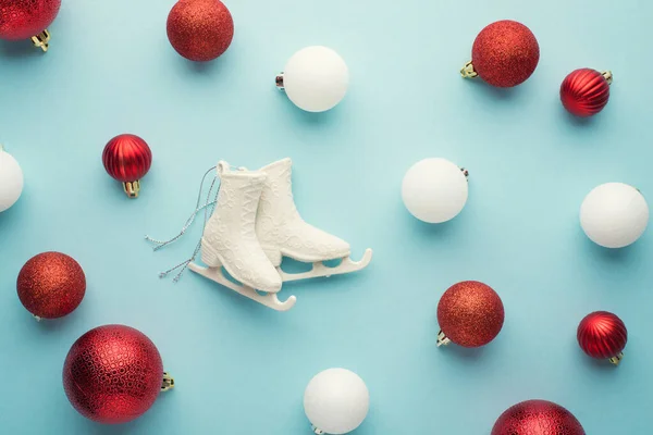 白色和红色圣诞树装饰球和小冰鞋在孤立的淡蓝色背景上的俯瞰照片 — 图库照片