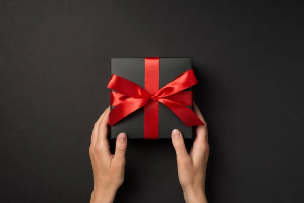 第一张手持黑色礼品盒的人的头像照片 礼品盒上有鲜艳的红丝带蝴蝶结 背景为孤立的黑色 — 图库照片
