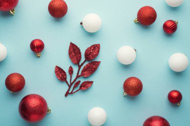 Beyaz ve kırmızı noel ağacı süsleme topları ve izole edilmiş pastel mavi arka plandaki dal parçalarının en üstteki fotoğrafı.