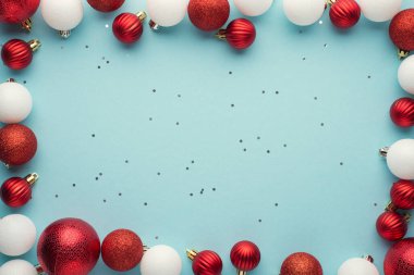 Beyaz ve kırmızı noel ağacı toplarının ve izole edilmiş pastel mavi arkaplandaki pulların en üstteki fotoğrafı. Ortasında boşluk var.