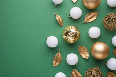 Altın ve beyaz noel ağacı küreleri ve altın yapraklarının izole edilmiş yeşil arka planda fotosu.