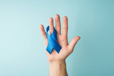 Mavi kurdeleli erkek eli ile prostat kanseri sembolünün izole edilmiş pastel mavi arka planda görüldüğü ilk kişi.