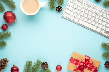 Çam kozalaklarından oluşan klavye fincanının en üstteki fotoğrafı kırmızı Noel ağacı topları ve kırmızı fiyonklu hediye kutusu ortadaki pastel mavi arka planda kopyalanmış boşluk