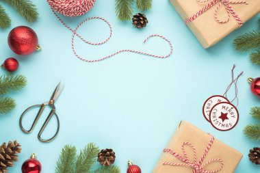 Çam ağaçlarının üst görüntüsü koni kırmızı noel ağacı makasları dekoratif ip makarası mutlu noel etiketleri ve izole edilmiş pastel mavi arkaplan üzerinde iki el işi kağıt hediye kutusu