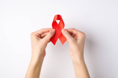 Üstten bakıldığında, kırmızı saten kurdele tutan genç bir kadının ellerinin fotoğrafı, izole edilmiş beyaz arka planda AIDS farkındalığının sembolü.