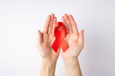Üstten bakıldığında, avuçlarında kırmızı ipek kurdele tutan genç bir kızın el fotoğrafı izole edilmiş beyaz arka planda AIDS farkındalığının sembolü.