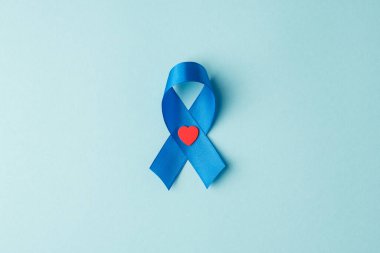 Mavi kurdele ve küçük kırmızı kalp sembolü prostat kanseri bilinci izole edilmiş pastel mavi arka planda.