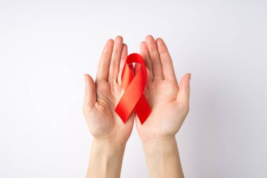 Avuçlarında kırmızı ipek kurdele tutan genç bir kadının el fotoğrafı izole beyaz arka planda AIDS farkındalığının sembolü.