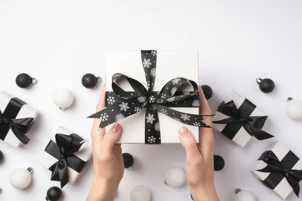 在第一张照片中 小女孩的手拿着黑色缎带的白色礼品盒 盖着礼物 白色和黑色的圣诞树球 白色的背景上空空如也 — 图库照片