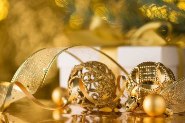 Noel atmosferi yaratıcı konsepti. Altın noel ağacı süslemelerinin yakın plan fotoğrafı... parlak altın bokeh arka planda serpentin kurdele... beyaz hediye kutusu ve çam dalı.