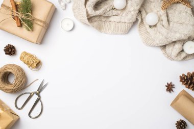 El işi kağıt hediye kutusunun en üstteki fotoğrafı çam dallı tarçın kurutulmuş limon dilimi eşarbı Noel ağacı topları sicim mumlarından makas makaraları ve kopyalanmış beyaz arka planda koniler