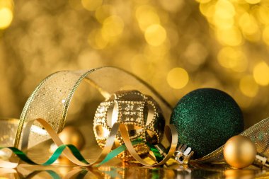 Altın ve yeşil Noel ağacı süslemelerinin yakın plan fotoğrafı altın bokeh arka planda topları yılanbalığı ve kurdeleyi süslüyor.