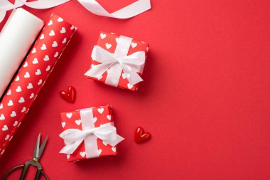 Kırmızı ambalaj kağıdındaki hediye kutularının en üstteki fotoğrafı kalplerin deseni ve beyaz kurdele yay küçük kalpler el işi aletler kağıt ve makas ruloları izole edilmiş kırmızı zemin