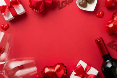 Sevgililer Günü süslemelerinin en üst görüntüsü hediye kutuları kalp şeklinde balonlar küçük kalpler izole edilmiş kırmızı arka planda iki şarap kadehi ve şarap şişesi ortada da kopyalanmış boşluk.