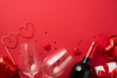 Sevgililer Günü süslemelerinin üst görüntüsü hediye kutusu kalp şeklinde kağıt bardaklar iki şarap şişesi ve kopyalanmış kırmızı arka planda kırmızı konfeti.