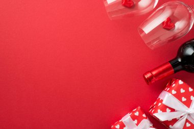 Sevgililer Günü süslemelerinin en üst görüntüsü kırmızı ambalaj kağıtlarıyla hediye kutuları içinde kalpler ve fiyonklar iki şarap kadehi ve şarap şişesinde küçük kalpler izole edilmiş kırmızı arka planda