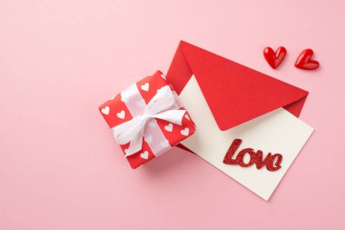 Sevgililer Günü dekorasyonunun en üst görüntüsü kırmızı zarf. Kartpostallı aşk hediyesi paketi kağıdı. İçinde kalplerin deseni ve izole edilmiş pastel pembe arka planda küçük kalpler var.