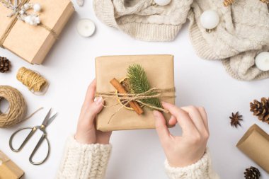 Süveter giymiş ellerin, kağıt hediye kutusundaki ip yayı çözerken çekilmiş fotoğrafı. Çam ağacından yapılmış tarçın dilimlenmiş limon dilimi eşarp topları üzerinde, el işi aletler izole edilmiş beyaz arka planda.