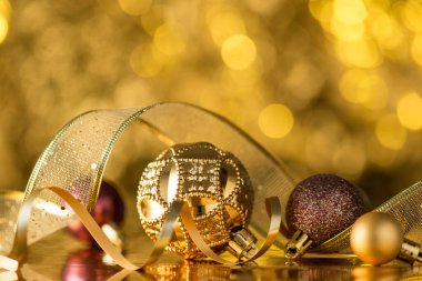 Altın ve kahverengi Noel ağacı süslemelerinin yakın plan fotoğrafı parlak altın bokeh arka planda toplar, yılanlar ve kurdeleler.