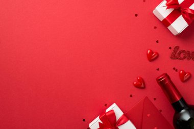 Sevgililer Günü süslemelerinin en üst görüntüsü beyaz hediye kutularında fiyonklu küçük kalpler yazılı aşk konfetisi ve şarap şişesi izole edilmiş kırmızı arka planda kopyalanmış