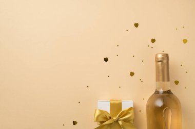 Sevgililer Günü dekorasyon kutusunun en üst görüntüsü altın kurdeleli altın pullu kalp şeklinde konfeti ve izole edilmiş bej arkaplanlı beyaz şarap şişesi.