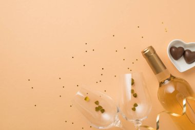 Sevgililer Günü 'nün en iyi görüntüsü kalp şekilli fincan tabağı çikolatalı şarap şişesi konfetili iki şarap kadehi ve izole edilmiş pastel bej arka plan ve kopyalanmış