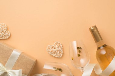 Sevgililer Günü 'nün en iyi görüntüsü, şarap şişesi, şarap kadehleri, kalp konfeti, ipek kurdele, kağıt hediye kutusu, izole edilmiş pastel bej arka planda beyaz oklu rattan kalpler.