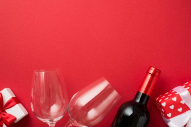 Sevgililer Günü dekorasyonunun en üst görüntüsü hediye kutuları iki şarap kadehi ve şarap şişesi ayrı kırmızı arka planda kopyalanmış