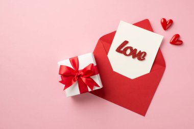 Sevgililer Günü süslemelerinin en üst görüntüsü küçük kalpler beyaz hediye kutusu kırmızı zarf açık kağıt kart ve yazılı aşk ile izole edilmiş pastel pembe arka plan
