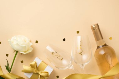 Beyaz gül sarısı ipek kurdele. Altın pullu iki şarap kadehi. Beyaz şarap şişesi. Kalp şeklinde konfeti ve izole edilmiş bej arka planda beyaz bir hediye kutusu.