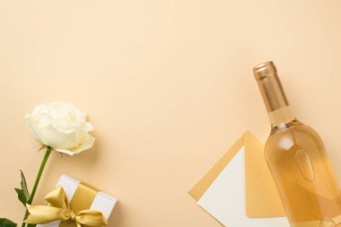 Üzerinde beyaz şarap şişesi ve kart olan beyaz şarap şişesinin en üstteki fotoğrafı ve kopyalanmış bej arka planda altın kurdeleli beyaz hediye kutusu.