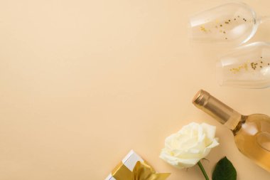 Sevgililer Günü süslemelerinin en üst görüntüsü beyaz gül, iki altın pullu şarap kadehi, altın yay ve izole edilmiş bej arka planda bir şişe beyaz şarap.