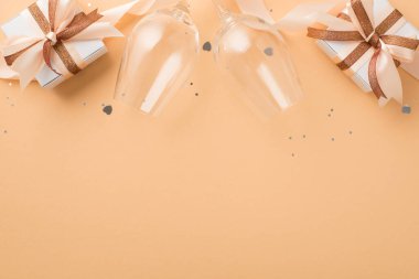 Sevgililer Günü dekorasyonunun en üst görüntüsü şarap gözlükleri parlayan kahverengi ve açık bej kurdeleli hediye kutuları izole edilmiş bej arka planda kalp şeklinde konfeti pulları ve boş alan.