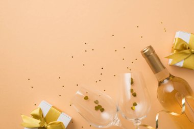 Sevgililer Günü süslemelerinin en üst görüntüsü altın fiyonklu beyaz hediye kutuları kalp şeklindeki şarap kadehleri ve izole edilmiş pastel bej arkaplanlı pullar.