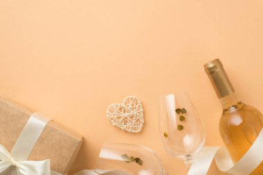 Sevgililer Günü 'nün en iyi fotoğrafı. Dekor şarap şişesi. Kalp şeklinde konfeti, rattan kalp kurdelesi, izole edilmiş pastel bej arka planda beyaz fiyonklu hediye kutusu.
