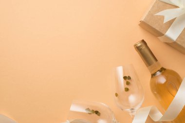 Sevgililer Günü dekorasyonunun en üst görüntüsü kalp şeklinde konfeti ipek kurdeleli şarap şişesi şarap bardakları ve izole edilmiş pastel bej arka planda beyaz fiyonklu kraft kağıt hediye kutusu.