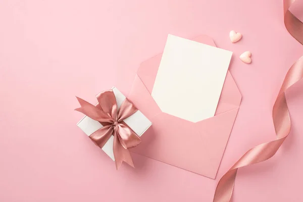 顶部照片白色礼品盒与粉红色弓形小红心卷曲丝带和开封粉红色信封与纸制卡片在孤立的粉红背景与空白空间 — 图库照片