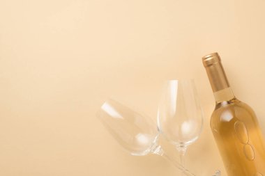 Top view photo of two wineglasses and bottle of white wine on isolated beige background with copyspace
