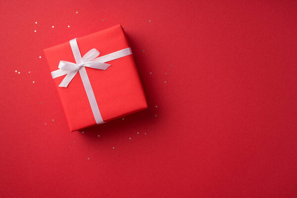 Top view photo of valentine's day decorations glowing sequins and red giftbox with white ribbon bow on isolated red background with copyspace