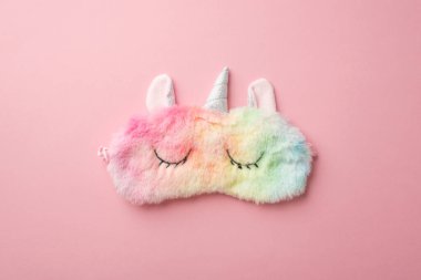 Top view photo of funny multicolored fluffy unicorn sleeping mask on isolated pastel pink background