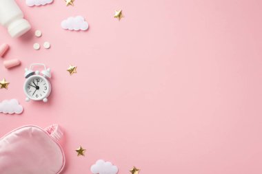 Top view photo of small white alarm clock pink silk sleeping mask bottle with pills earplugs golden stars and clouds on isolated pastel pink background with blank space