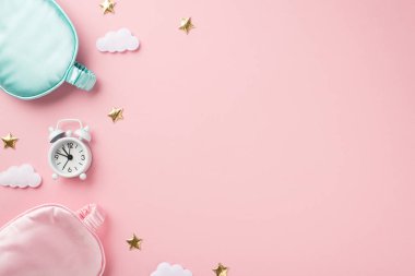 Top view photo of small white alarm clock pink and blue silk sleeping masks golden stars and clouds on isolated pastel pink background with empty space