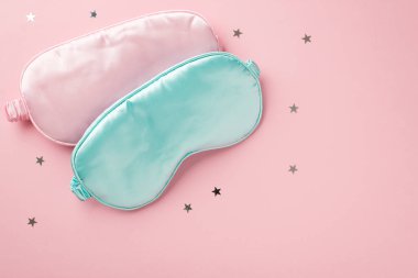 Top view photo of two light pink and blue silk sleeping masks and star shaped confetti on isolated pastel pink background with empty space