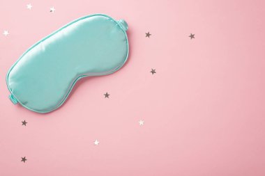 Top view photo of blue silk sleeping mask and star shaped confetti on isolated pastel pink background with copyspace