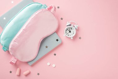 Top view photo of two blue and pink silk sleeping masks small white alarm clock pills earplugs blue reminder and star shaped confetti on isolated pastel pink background with empty space