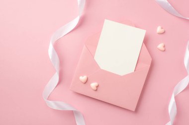 Top view photo of open pink envelope with paper sheet small pink hearts and white ribbon on isolated pastel pink background with copyspace